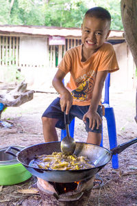 Portrait of boy preparing food while sitting on chair in yard