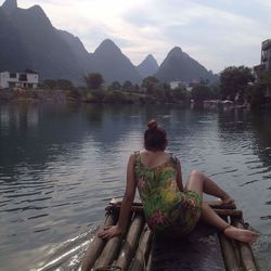 Rear view of friends sitting on lake against mountains