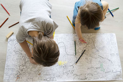High angle view of siblings drawing in book on floor at home