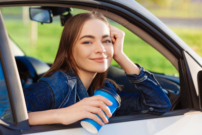 Beautiful young woman traveled on road in car, drinking coffee from disposable