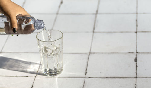 Pouring water from bottle into glass on a table made of white tiles