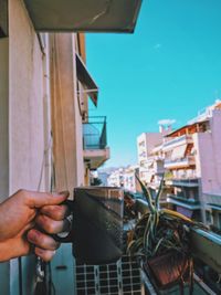 Midsection of person holding umbrella in city against sky