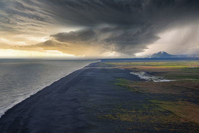 Scenic view of beautiful black sand beach against cloudy sky during sunset