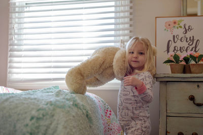 Portrait of cute girl holding stuffed toy while standing at home