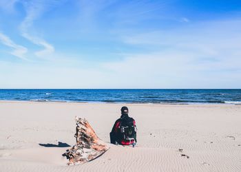 Man sitting at beach against sky during sunny day