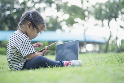 Young woman using laptop while sitting on field