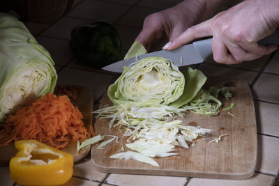 A woman cuts cabbage in the kitchen against the background of fresh vegetables