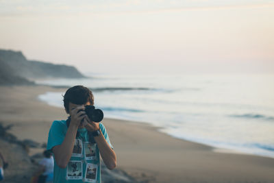 Man photographing with digital camera at beach during sunset