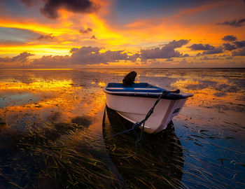 Boat moored on beach against sky during sunset
