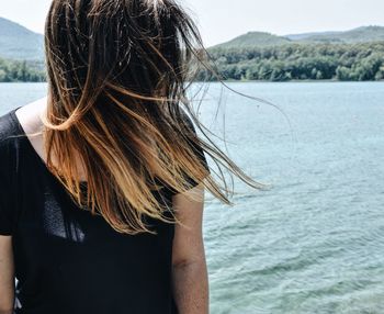 Woman with tousled blond hair against sea on sunny day