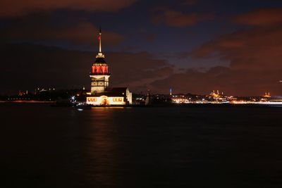 Illuminated building by sea against sky at night