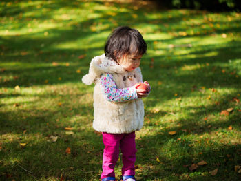 Baby girl holding apple while standing on grassy field at park