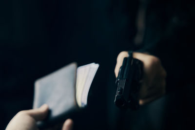 Close-up of hand holding book against black background