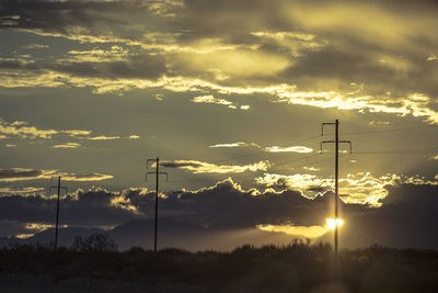 Silhouette electricity pylon against dramatic sky during sunset