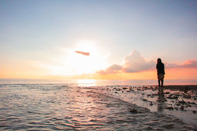 Silhouette woman standing at beach against sky during sunset