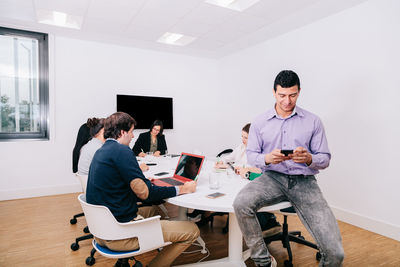 Businessman using phone while coworkers working by conference table