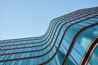 Modern building with curved glass facade reflecting sky.