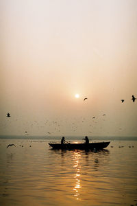 Silhouette birds on sea against sky at sunset