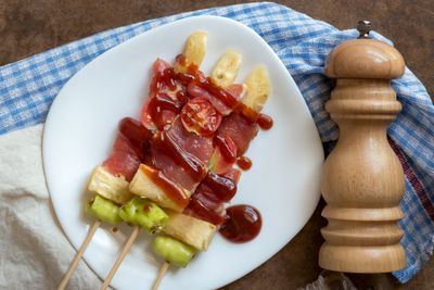 Directly above shot of food in skewers on plate with pepper bottle