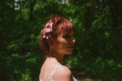 Close-up of young woman looking away while standing against trees