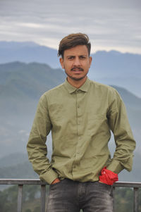 A young guy looking at camera with hands in pocket while standing against the background of mountain