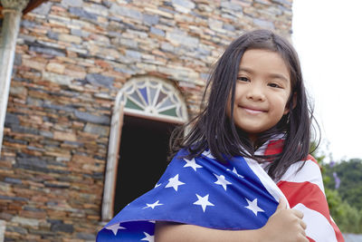 Portrait of smiling girl wearing american flag against building