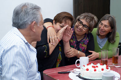 An older man with his friends celebrating his birthday, laughing and playing at an indoor party.