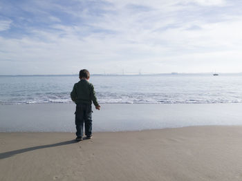 Rear view of boy standing on shore at beach