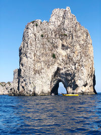 Rock formation by sea against clear blue sky