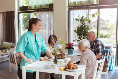 Female caregiver serving meal to senior people in nursing home