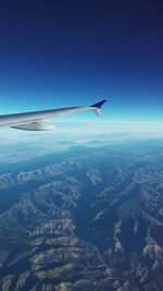 Aerial view of airplane flying over landscape against blue sky