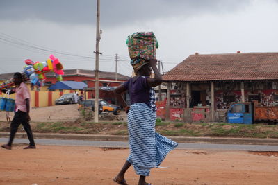 Rear view of people walking on house against sky