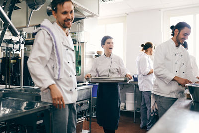 Smiling female chef with colleagues working in commercial kitchen