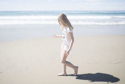 Full length side view of girl holding stone while walking at beach