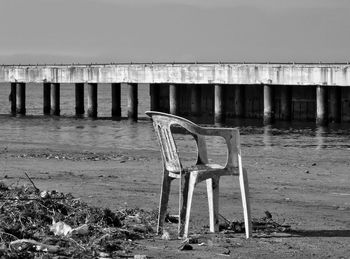 Abandoned chair on shore at beach against sky