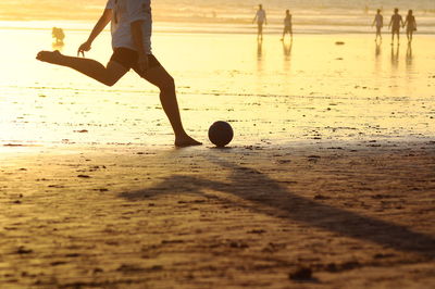 Low section of man playing soccer at beach during sunset