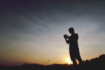 Silhouette man photographing against sky during sunset