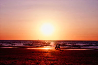 Silhouette people walking at beach against sky during sunset