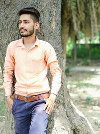 Portrait of young man standing against tree trunk