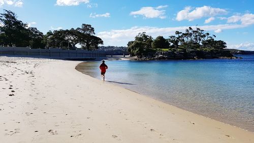 Rear view of man walking on beach against sky