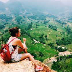 High angle view of hiker sitting on cliff while looking at terraced field