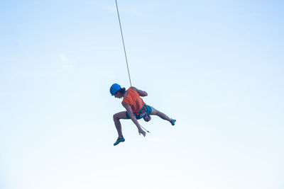 Low angle view of man swinging from rope against clear sky