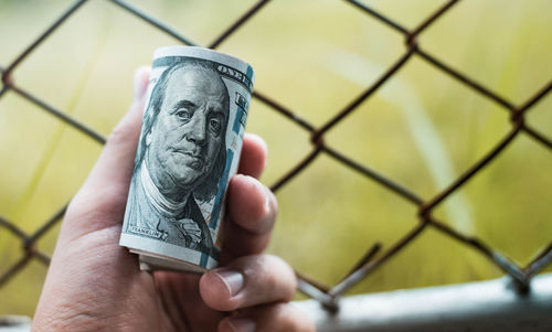 Cropped hand of man holding currency by fence