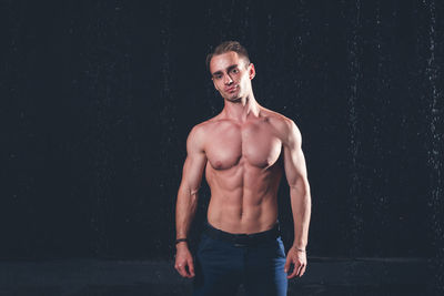 Portrait of shirtless man standing against black background