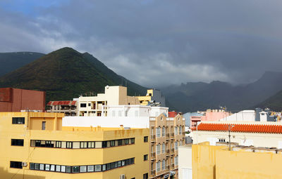 Residential buildings by mountains against cloudy sky at san sebastian de la gomera