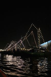 Illuminated suspension bridge over river against sky at night