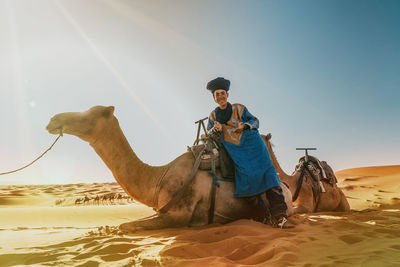 Man riding horse in desert against sky