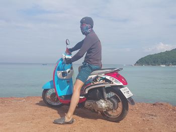 Man riding motorcycle on sea against sky