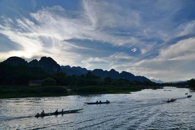 Silhouette people in boats on river against sky at sunset