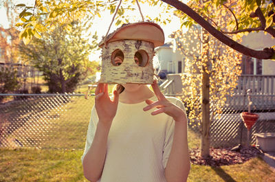 Portrait of boy holding camera while standing against tree